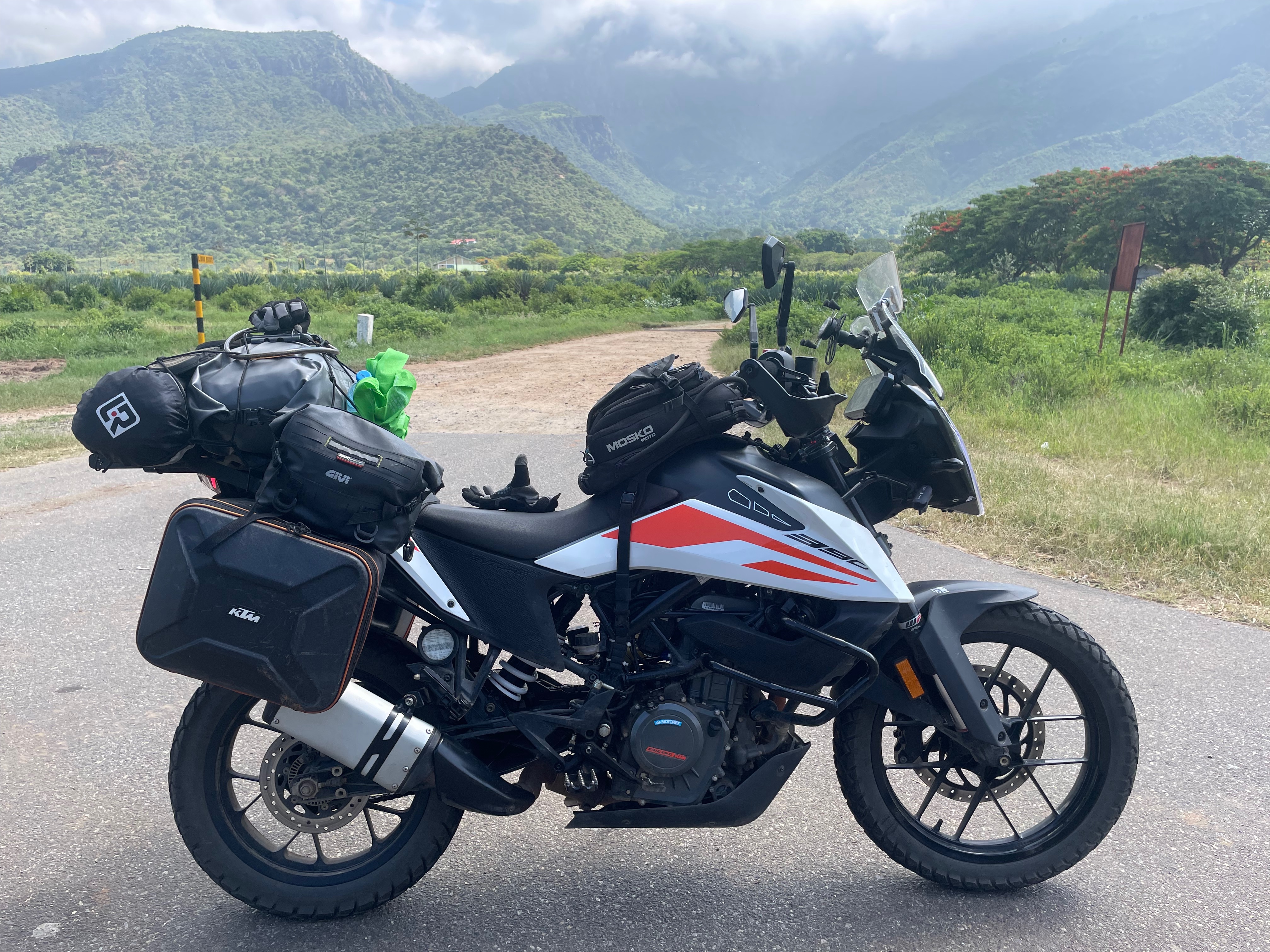 A KTM 390 Adventure loaded with gear parked on a road with mountainous scenery in the background. Tanzania